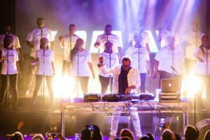 A group of people performing on stage with DJ equipment, creating an energetic atmosphere for the audience.