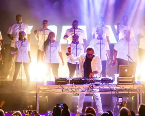 A group of people performing on stage with DJ equipment, creating an energetic atmosphere for the audience.