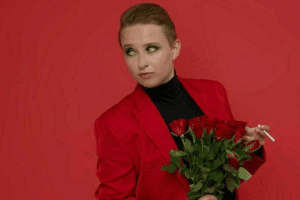 A woman in a red suit stands confidently, holding a vibrant bouquet of roses in her hands.