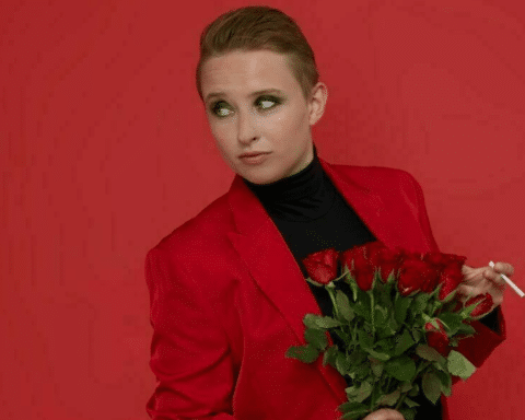 A woman in a red suit stands confidently, holding a vibrant bouquet of roses in her hands.