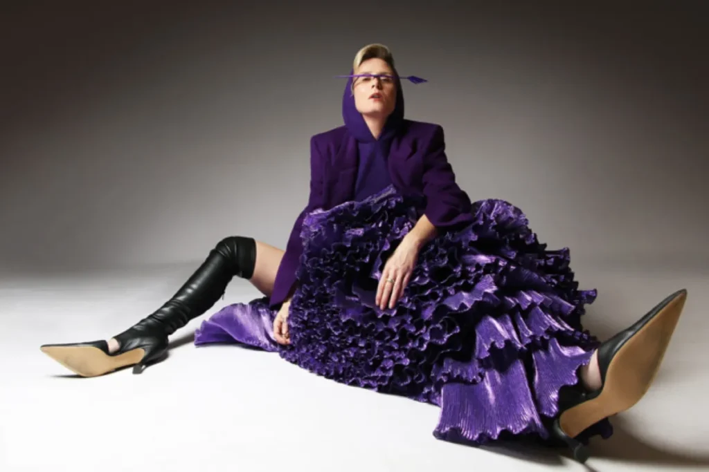 A woman in a purple dress sits gracefully on the floor, exuding elegance and calmness in her pose.