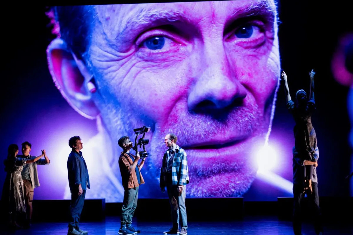 A group of people stands on stage in front of a large screen displaying a man.