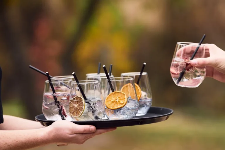 A person holding a tray filled with drinks, each garnished with a slice of lemon.